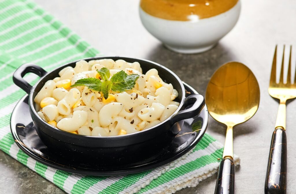 A delicious serving of creamy macaroni pasta with corn garnished with herbs in a black bowl.